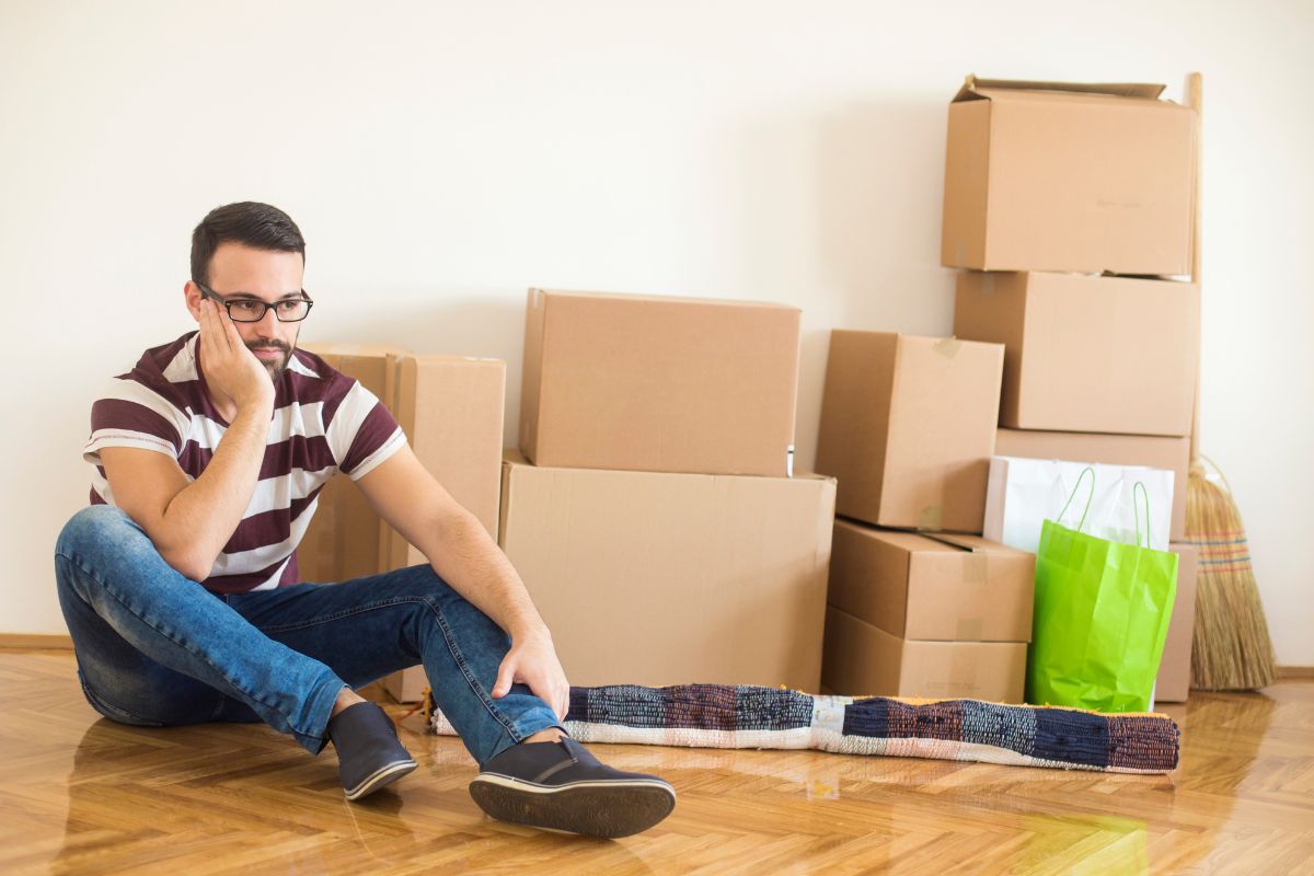 Even good life transitions, such as moving to a new home, can affect how you feel internally. - Picture of tired frustrated man sitting on floor next to moving boxes.