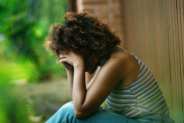 Woman grieving. - Image shows a young woman sitting outdoors with her head in her hands and has a seen of grief