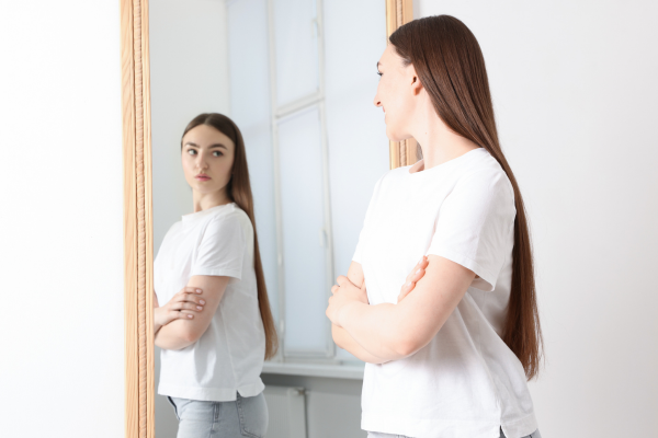 Woman being self-critical of herself while looking in a mirror.