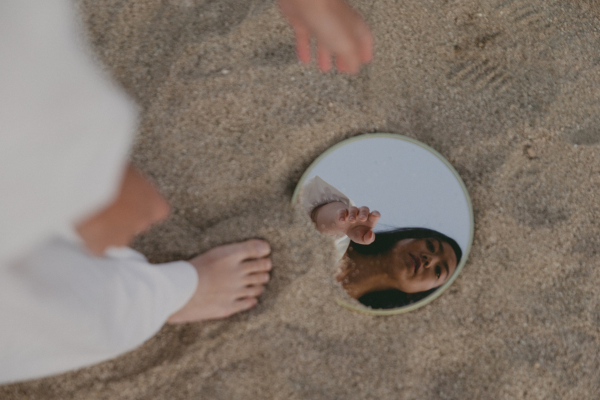identity changes - woman looking in mirror in sand
