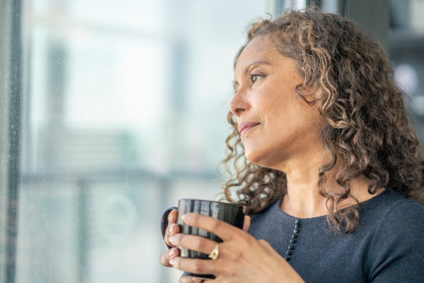 Woman contemplating why she has negative thoughts. - woman holds coffee cup while looking out the window