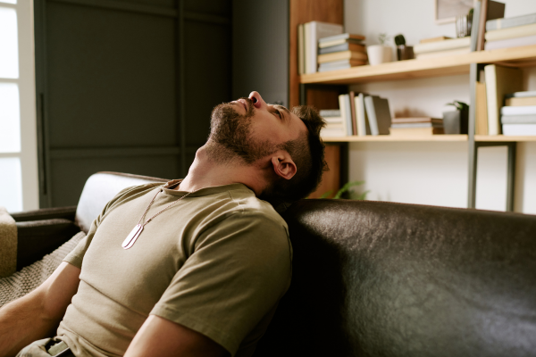 Man sitting on couch with head leaning back showing fatigue and emotional exhaustion.