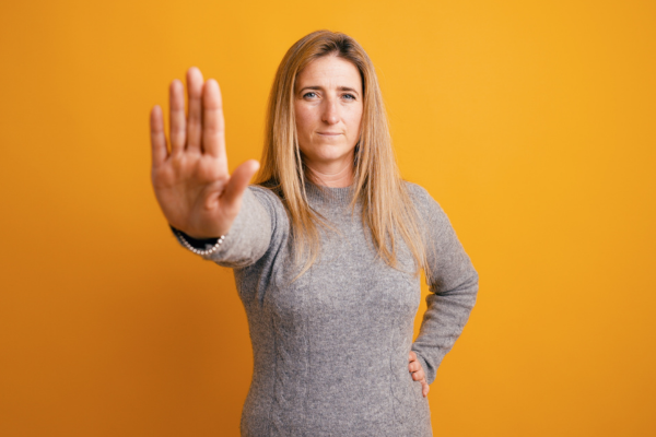 Woman holding out hand to say "no" to more things to do...creating boundaries for her people pleasing tendency